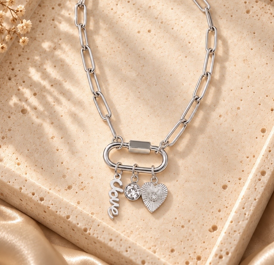 Silver Love, Always paperclip-chain charm necklace with script love, crystal, and textured heart charms arranged on a tray