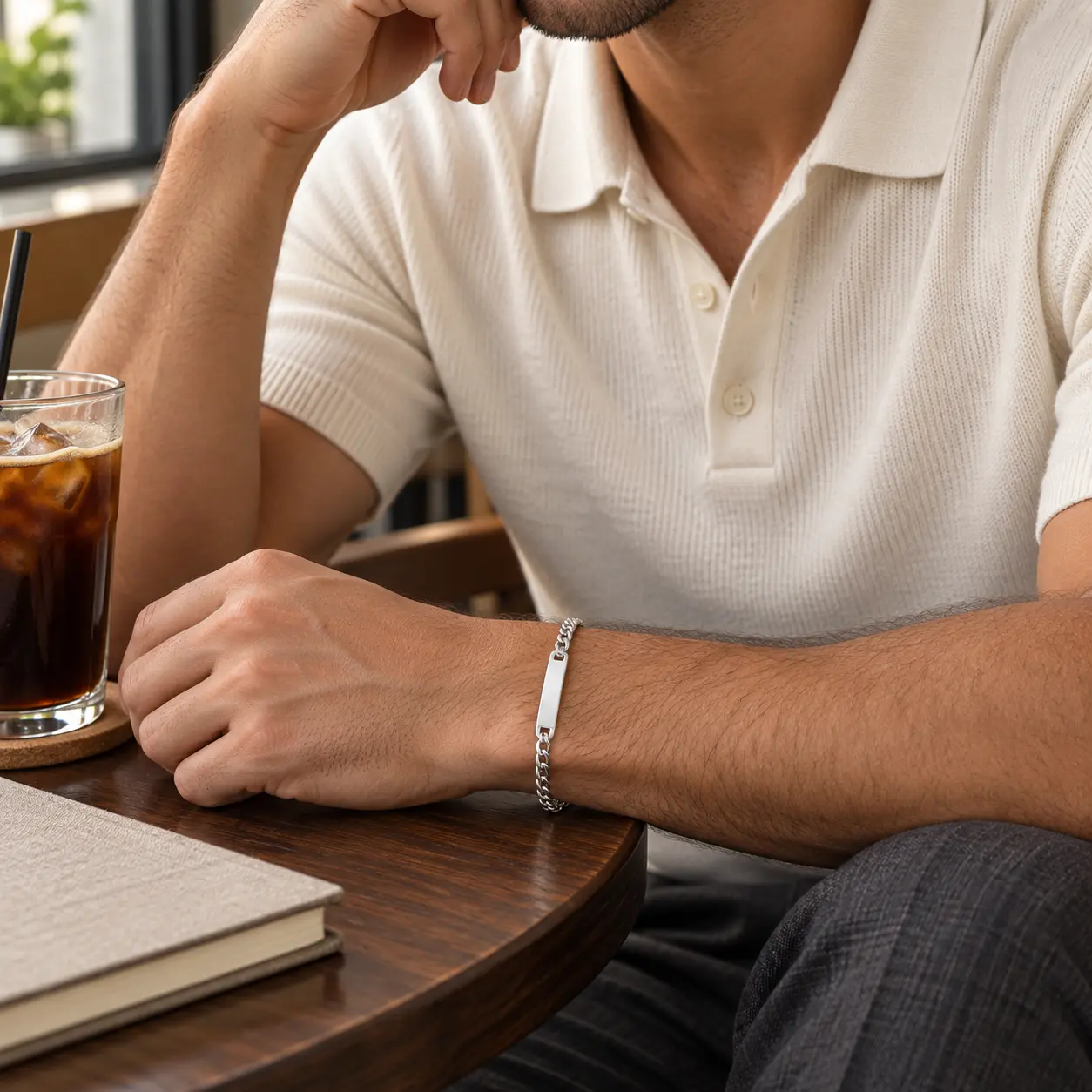 Man wearing a slim silver Men’s Classic ID Bracelet with a rectangular engraving bar at a café table